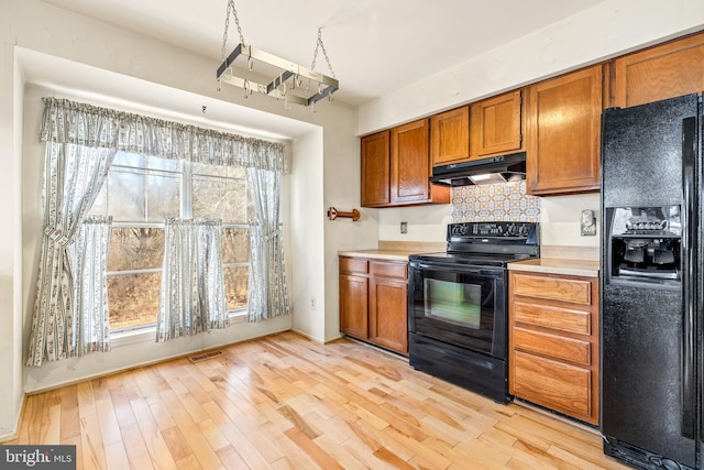 kitchen featuring black appliances, brown cabinetry, a wealth of natural light, and under cabinet range hood