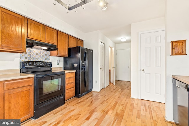 kitchen with under cabinet range hood, light wood-style floors, light countertops, black appliances, and brown cabinetry