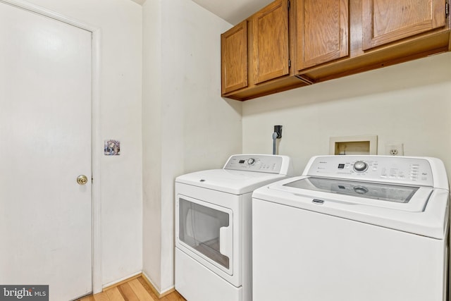 clothes washing area with cabinet space, light wood-style flooring, and washer and dryer