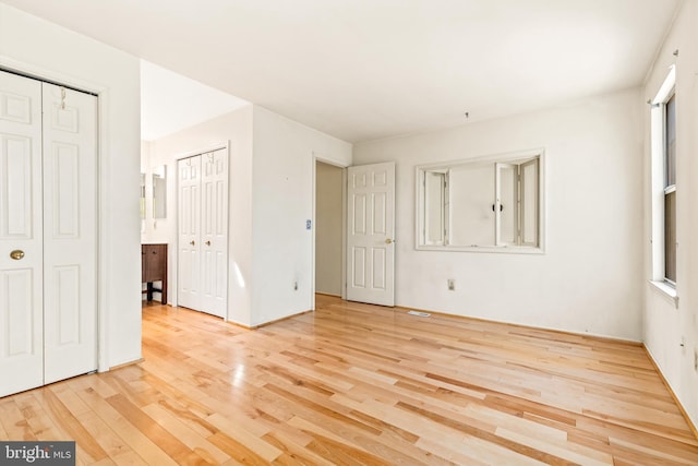 unfurnished bedroom featuring wood finished floors and two closets