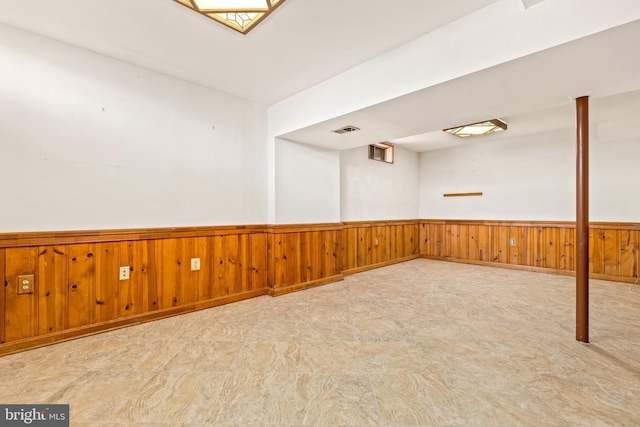 empty room featuring wooden walls, a wainscoted wall, and visible vents