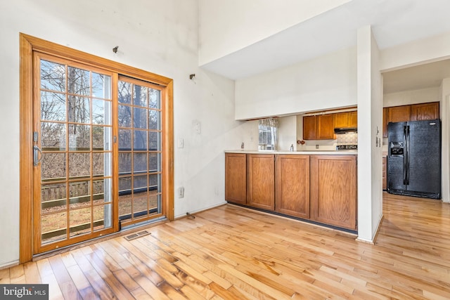 kitchen with visible vents, brown cabinetry, black fridge with ice dispenser, a high ceiling, and light wood-style floors