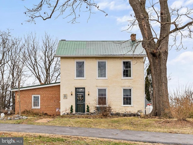 view of front of home with brick siding, metal roof, and a chimney