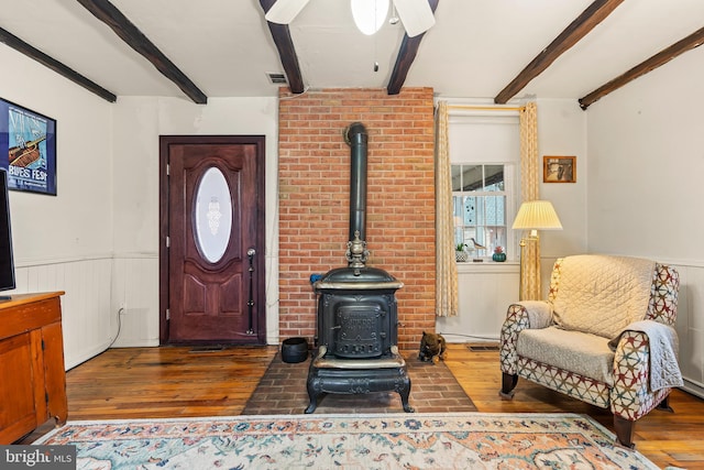 living area featuring beam ceiling, wainscoting, wood finished floors, and a wood stove