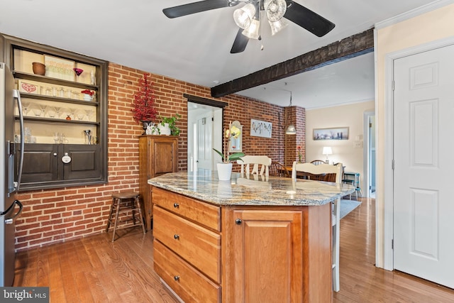 kitchen with light stone counters, a breakfast bar, beam ceiling, wood-type flooring, and brick wall