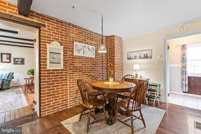 dining room with hardwood / wood-style flooring, brick wall, and ornamental molding