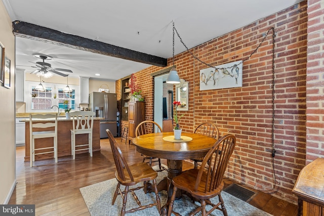 dining room featuring light wood finished floors, visible vents, brick wall, ceiling fan, and beamed ceiling