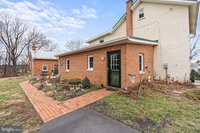 back of house with brick siding and a chimney