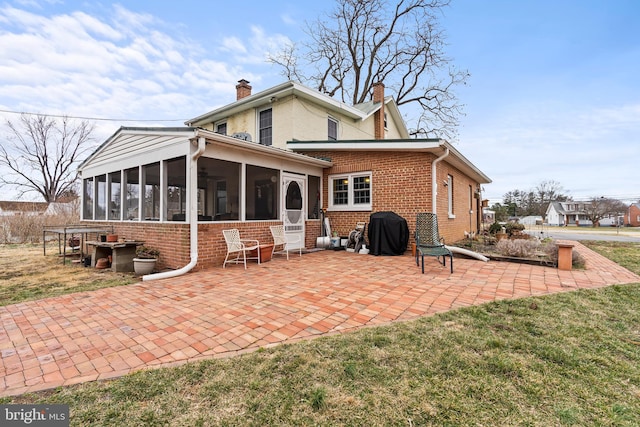 back of house featuring a sunroom, a patio area, brick siding, and a chimney