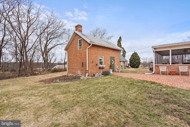 exterior space with a patio, brick siding, a sunroom, a lawn, and a chimney