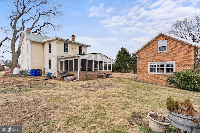 rear view of house with a yard, brick siding, a chimney, and a sunroom