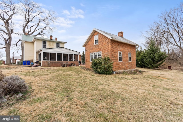 rear view of property featuring a lawn, brick siding, a chimney, and a sunroom