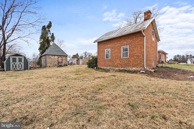 view of home's exterior featuring a storage shed, a chimney, an outbuilding, a yard, and brick siding