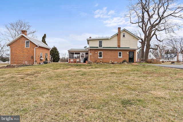 back of property with a sunroom, brick siding, a yard, and a chimney