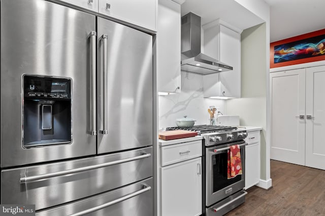 kitchen with dark wood-style flooring, stainless steel appliances, backsplash, white cabinetry, and wall chimney range hood