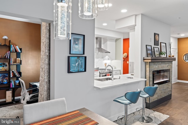 kitchen with baseboards, wall chimney exhaust hood, wood finished floors, a fireplace, and a sink