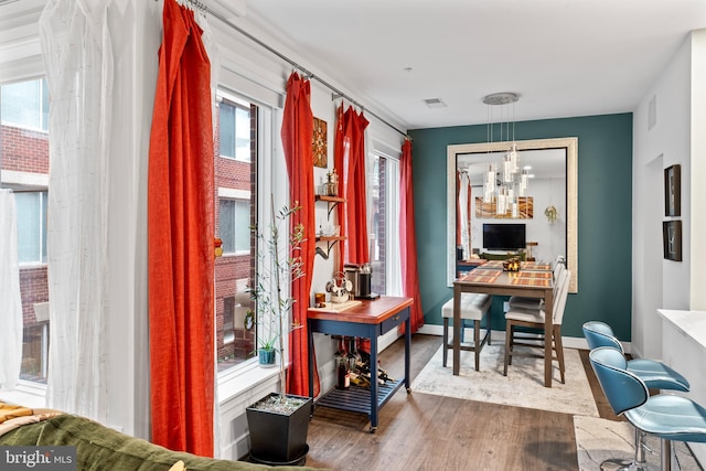 office space featuring a chandelier, wood finished floors, visible vents, a healthy amount of sunlight, and baseboards