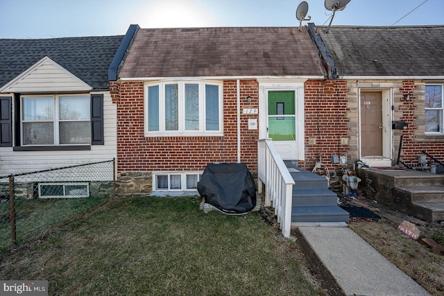 townhome / multi-family property featuring brick siding, a shingled roof, a front yard, and fence