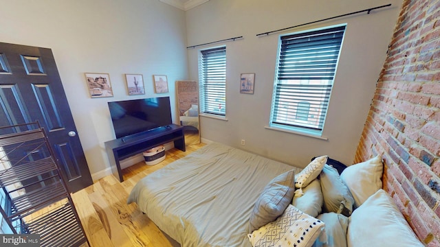 bedroom with crown molding, brick wall, wood finished floors, and baseboards