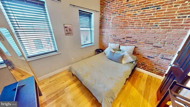 bedroom featuring baseboards, brick wall, and wood finished floors