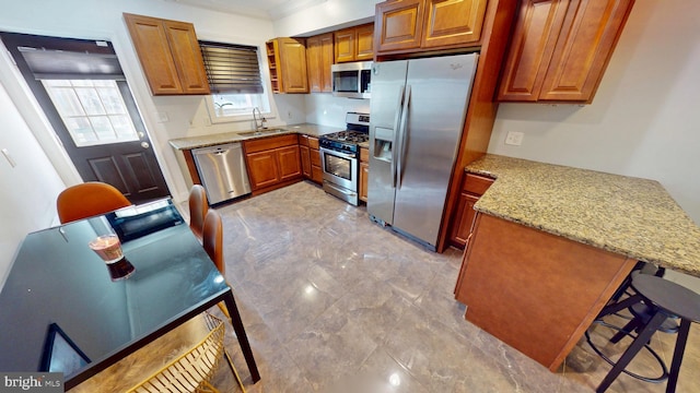 kitchen with stainless steel appliances, a peninsula, a sink, and brown cabinets