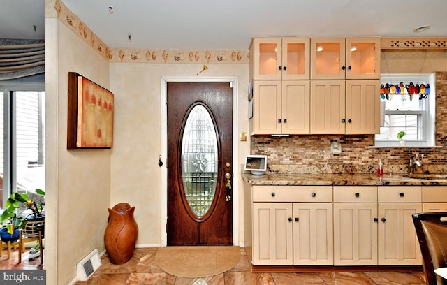 kitchen featuring visible vents, backsplash, glass insert cabinets, a sink, and light stone countertops