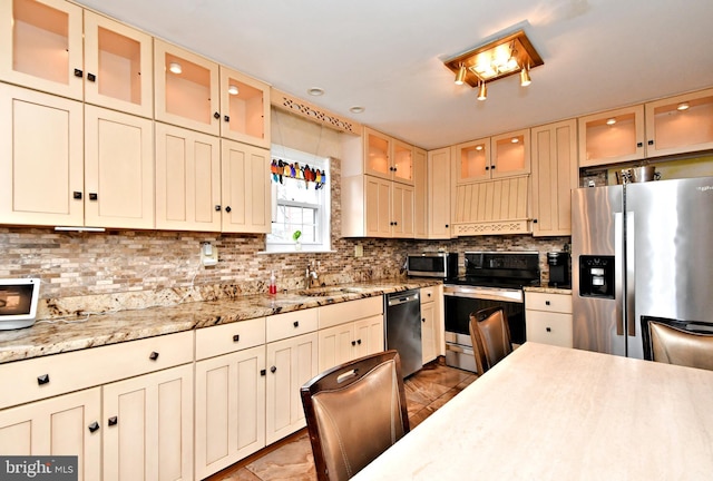 kitchen featuring cream cabinetry, tasteful backsplash, custom range hood, appliances with stainless steel finishes, and glass insert cabinets