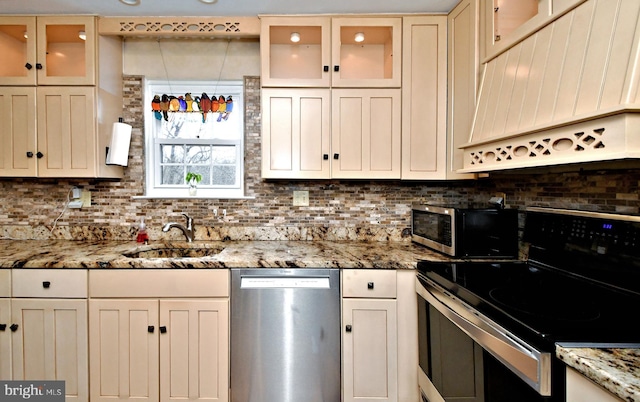 kitchen featuring premium range hood, a sink, appliances with stainless steel finishes, tasteful backsplash, and glass insert cabinets