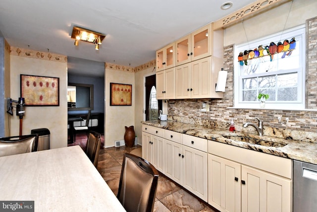 kitchen with visible vents, decorative backsplash, dishwasher, glass insert cabinets, and a sink