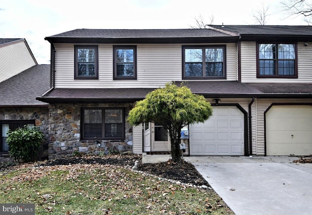 view of property featuring stone siding, concrete driveway, roof with shingles, and an attached garage