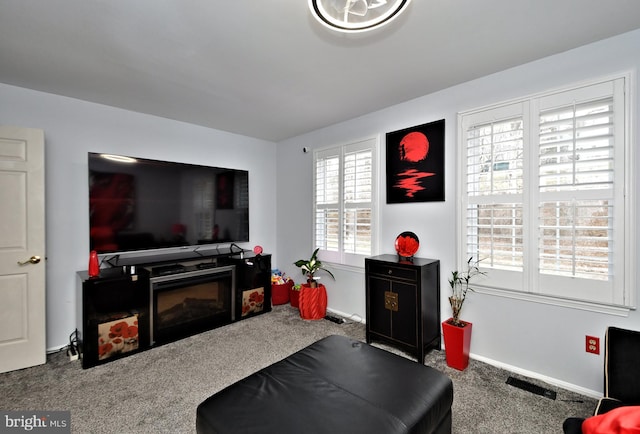 carpeted living room featuring a glass covered fireplace, visible vents, and baseboards