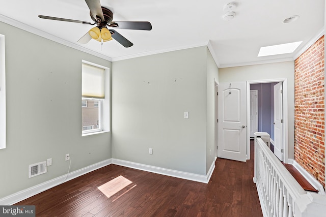 unfurnished room with a skylight, dark wood-style flooring, visible vents, and crown molding