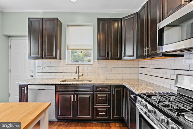 kitchen with appliances with stainless steel finishes, dark wood-type flooring, ornamental molding, a sink, and light stone countertops