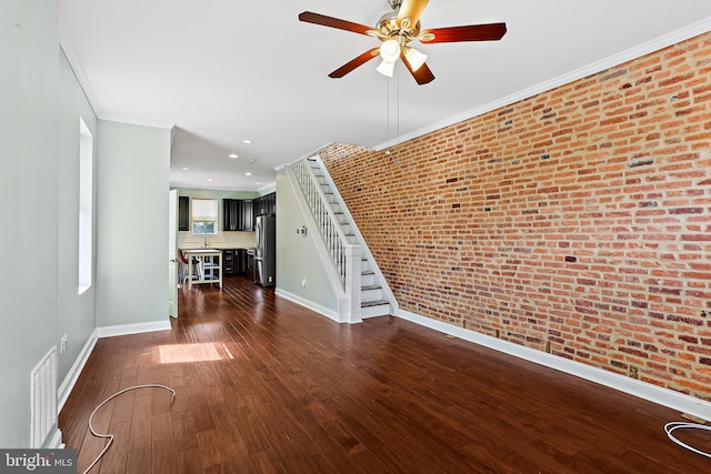 unfurnished living room featuring dark wood-style floors, crown molding, visible vents, stairway, and brick wall