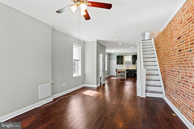 unfurnished living room with dark wood finished floors, visible vents, brick wall, baseboards, and stairs