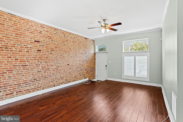 spare room with ceiling fan, brick wall, dark wood-type flooring, baseboards, and crown molding