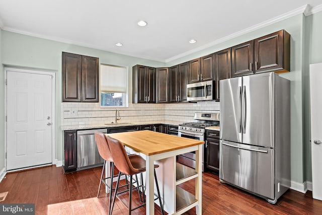 kitchen with dark brown cabinetry, butcher block countertops, a sink, appliances with stainless steel finishes, and dark wood finished floors