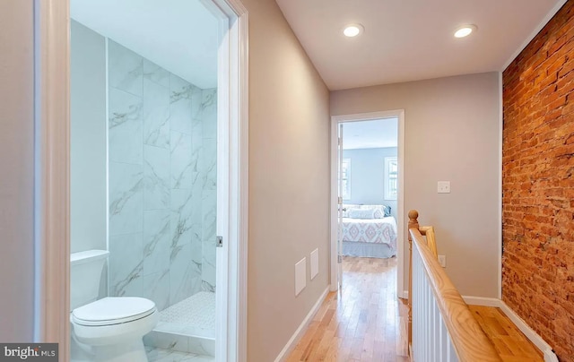 ensuite bathroom featuring toilet, brick wall, wood finished floors, baseboards, and a marble finish shower