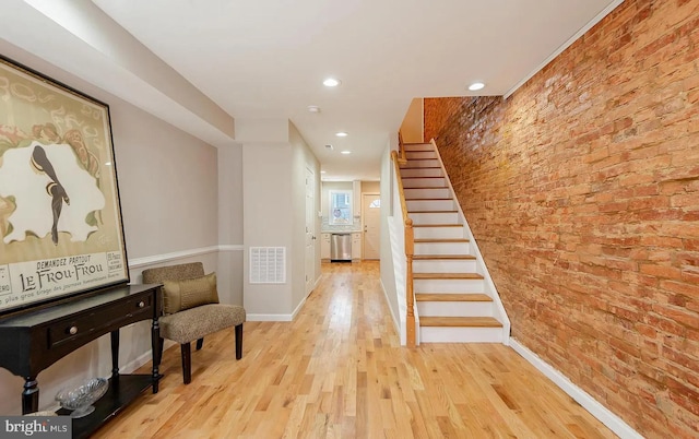 hall with visible vents, baseboards, light wood-style flooring, brick wall, and stairway