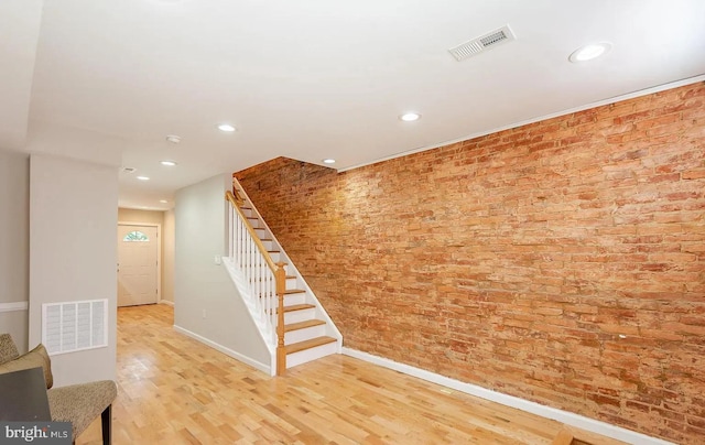 interior space featuring baseboards, visible vents, brick wall, and wood finished floors