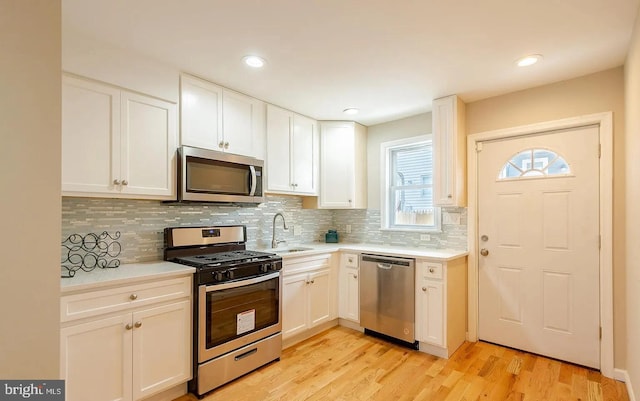 kitchen with light wood-style flooring, a sink, white cabinetry, light countertops, and appliances with stainless steel finishes