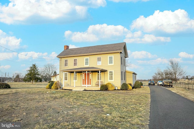 view of front of property with covered porch, a chimney, a front yard, and fence