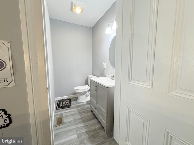 half bathroom featuring baseboards, visible vents, toilet, wood finished floors, and vanity