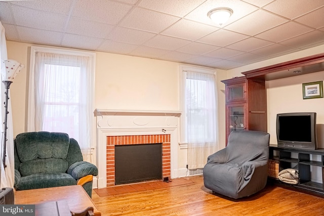 living area with a brick fireplace, wood finished floors, and a paneled ceiling