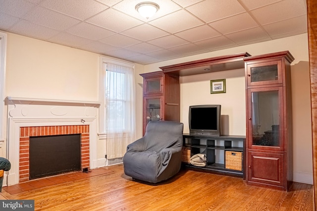 living area featuring a paneled ceiling, light wood finished floors, and a fireplace