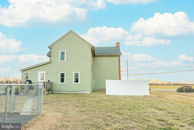 rear view of property with a chimney, fence, and a lawn