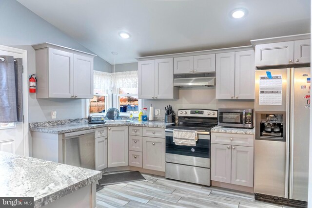 kitchen with vaulted ceiling, stainless steel appliances, light countertops, and under cabinet range hood