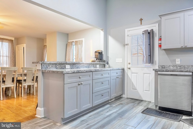 kitchen with light stone counters, gray cabinetry, a peninsula, dishwasher, and light wood finished floors