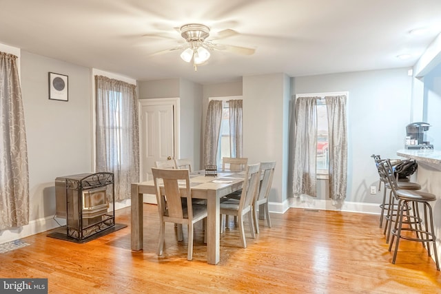 dining area featuring a wood stove, ceiling fan, light wood-style flooring, and baseboards