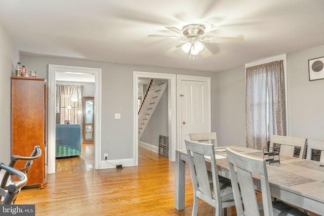 dining space with stairs, light wood-type flooring, a ceiling fan, and baseboards